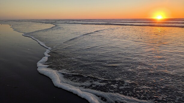 Ein Strand mit Sonnenuntergang, Wellen und klarem Himmel.