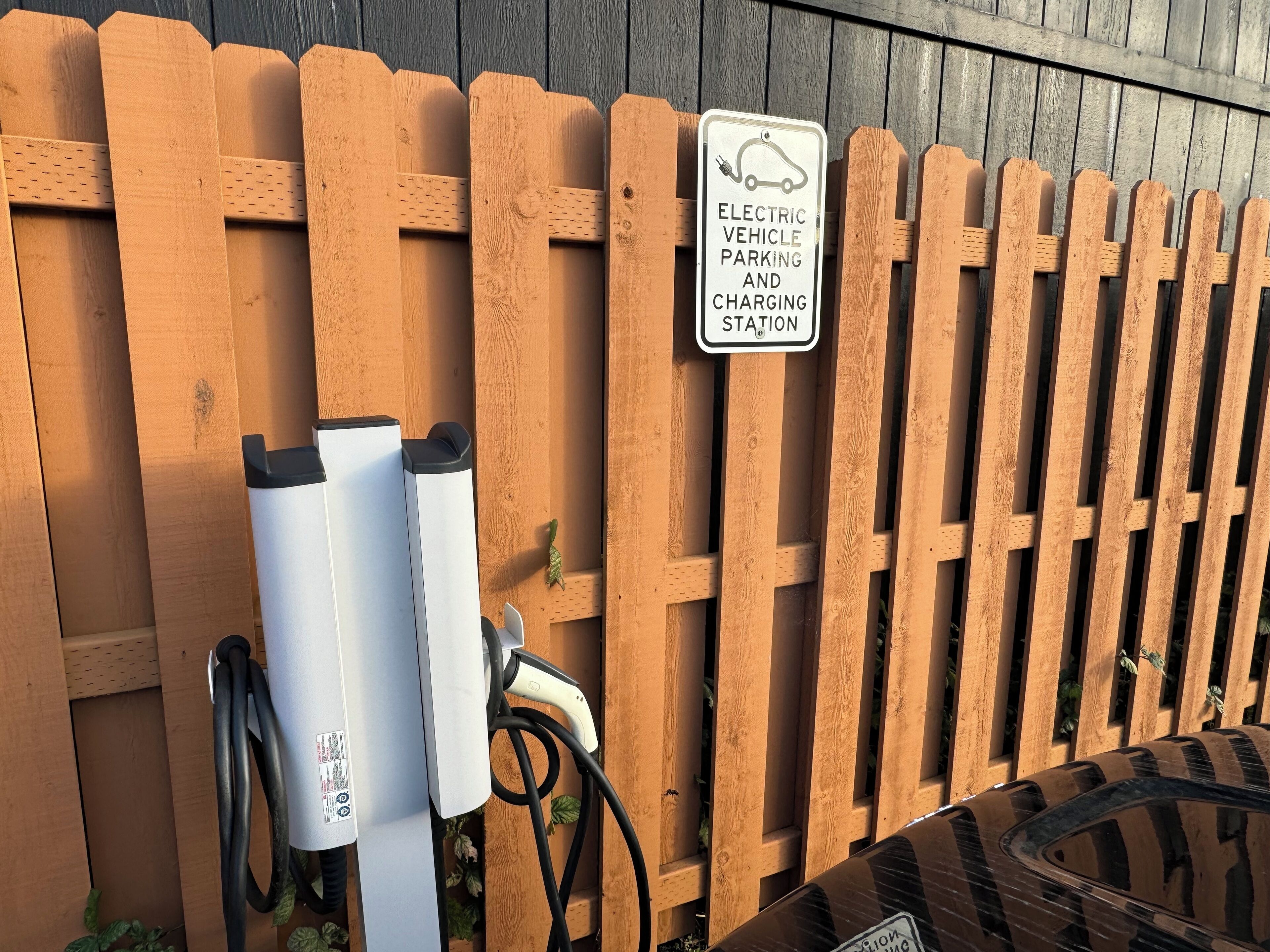 A wooden fence with an electric vehicle charging station and a sign indicating its purpose.