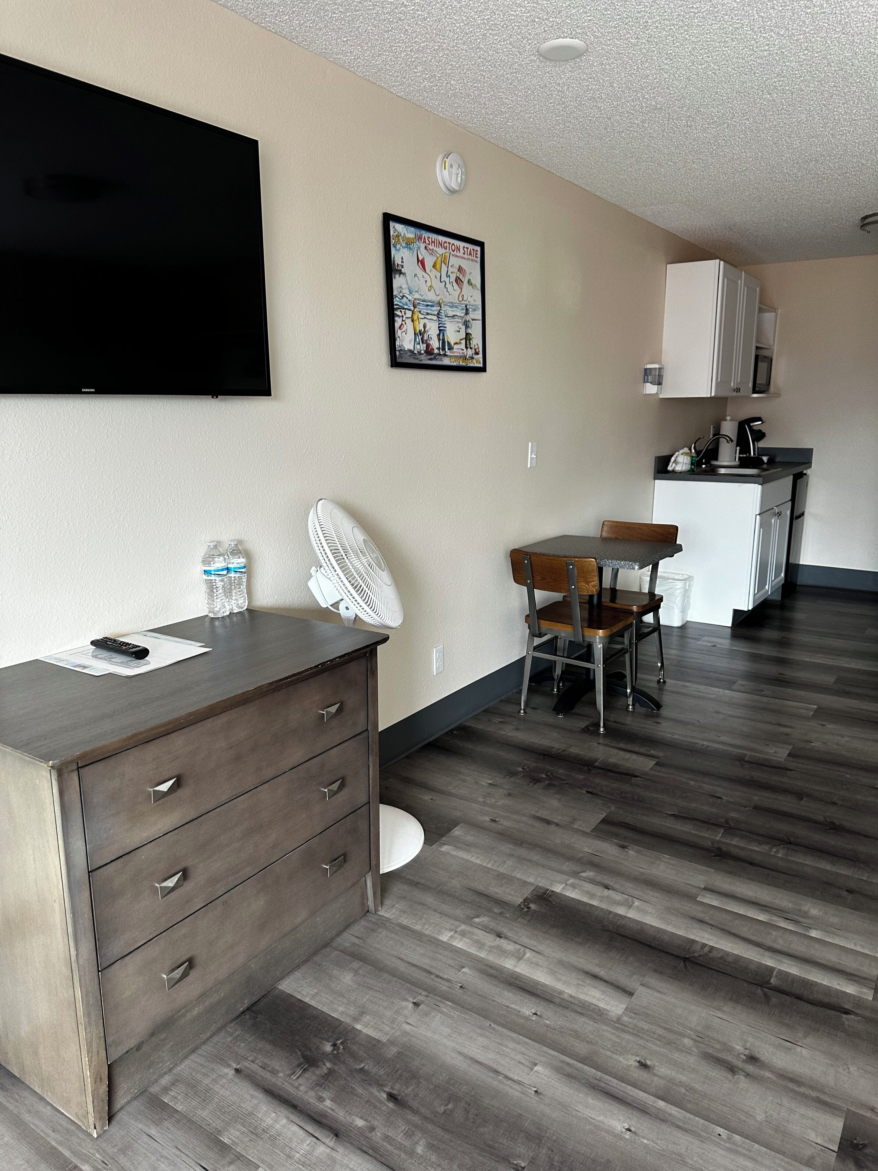 A compact living space with a kitchenette, a dining area, and a flat-screen TV mounted on the wall.