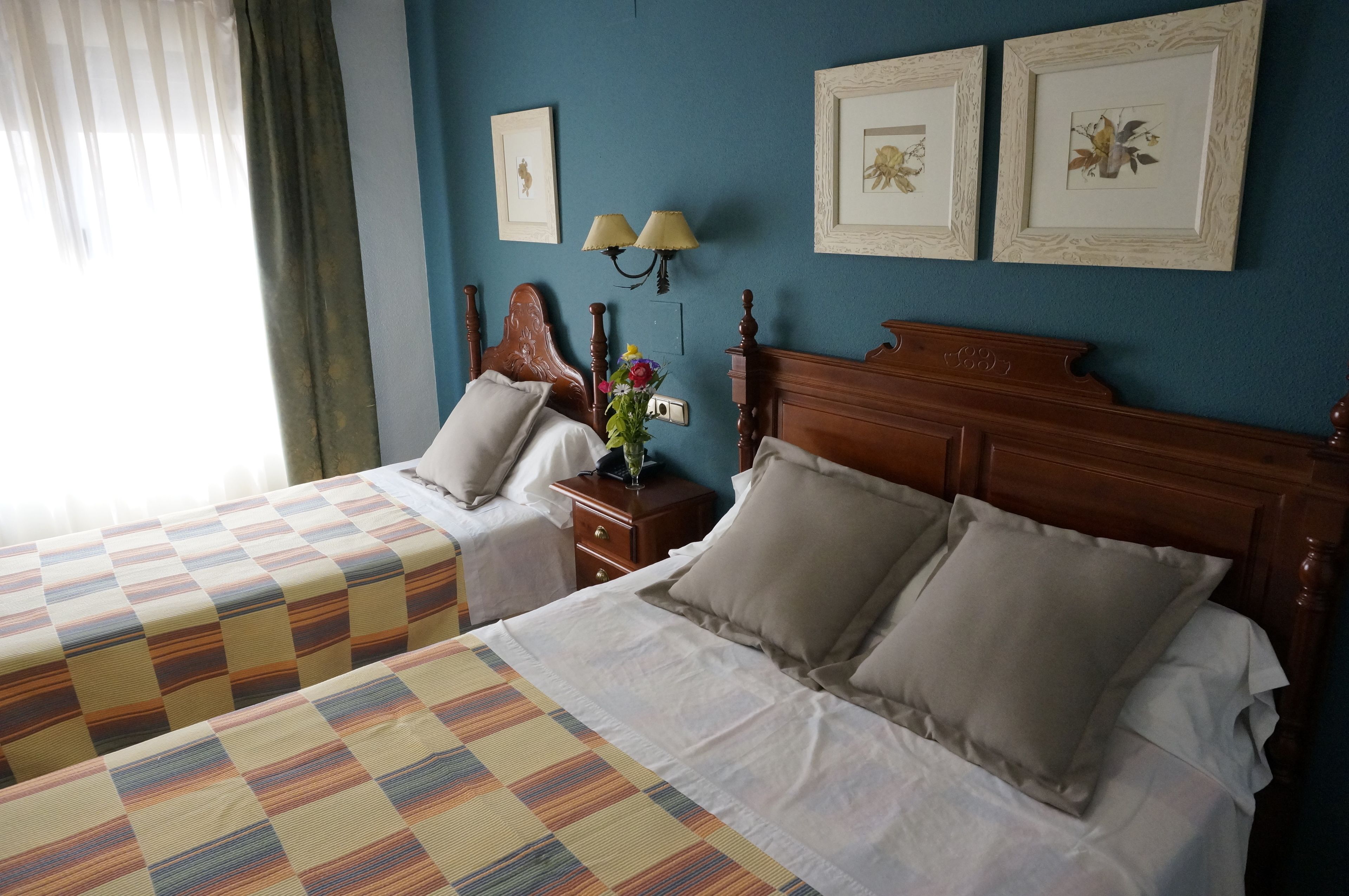Een hotelkamer met twee bedden, een houten hoofdeinde, een nachtkastje met een lamp, en lijstwerken aan de muur.