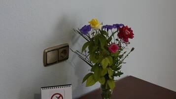 A wooden table with a bouquet of flowers, a framed picture, a wall-mounted lamp, a no-smoking sign, and a thermostat.