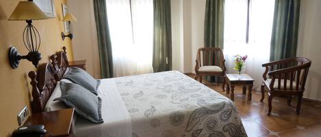 A hotel room with a bed, two chairs, a small table, and a lamp.