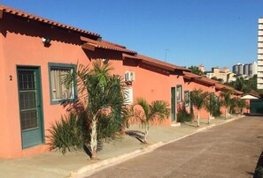 Una hilera de edificios anaranjados con puertas y ventanas verdes, bordeada por pequeñas palmeras.