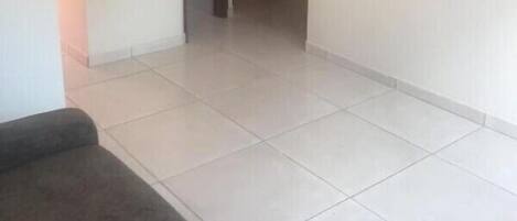 Una habitación con un sofá oscuro, un televisor de pantalla plana en la pared y piso de baldosas.