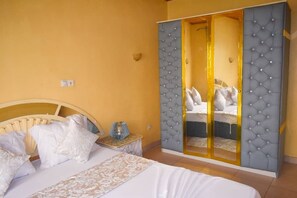 A bedroom with a bed, a nightstand, and a wardrobe with a mirror. - Résidence hôtelière Borel Douala (Douala)