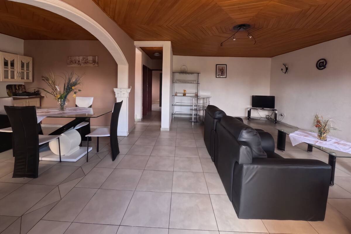 Un grand espace de vie doté d’un plafond en bois, d’une table à manger avec des chaises, d’un canapé et d’un téléviseur.