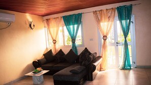 A living room with a sofa, a small table with a plant, and curtains on the windows. - Résidence hôtelière Borel Douala (Douala)