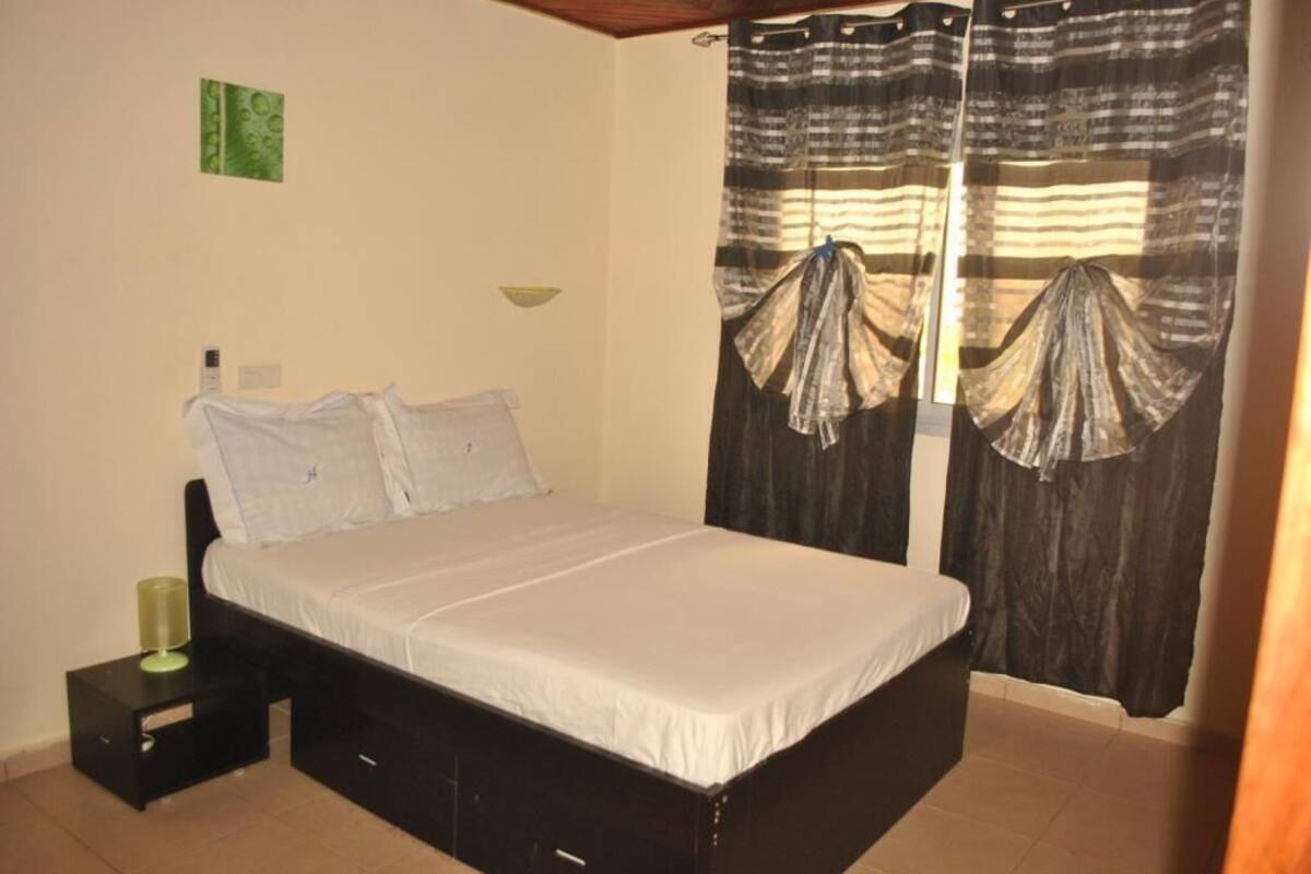 Une chambre à coucher avec un lit, une table de chevet, une lampe fixée au mur et des rideaux.