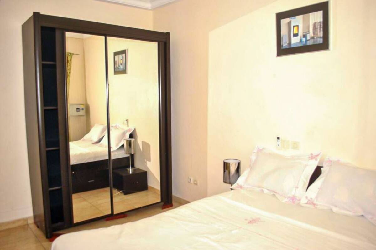 Une chambre à coucher comprenant un lit, une armoire avec un miroir, une table de chevet et un tableau accroché au mur.