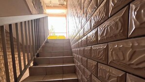 A staircase with a textured wall on one side and a metal railing on the other, leading to a bright room with a yellow wall. - Résidence hôtelière Borel Douala (Douala)
