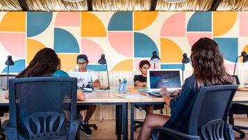 Un grupo de personas sentadas alrededor de una mesa con portátiles, en una sala con un llamativo diseño geométrico en la pared.