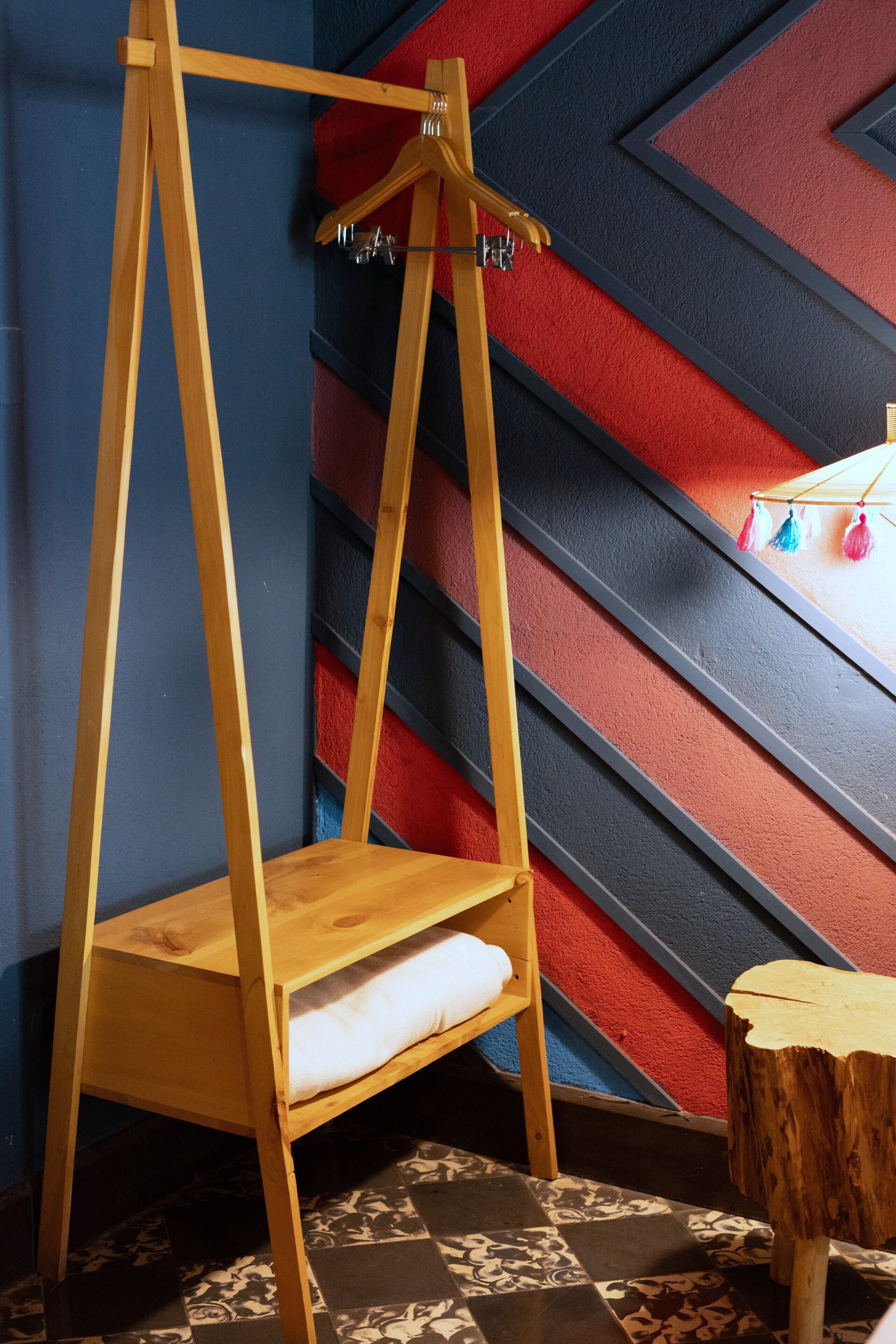 Una silla mecedora de madera con un cojín blanco, un taburete de madera y una pared con un diseño geométrico.