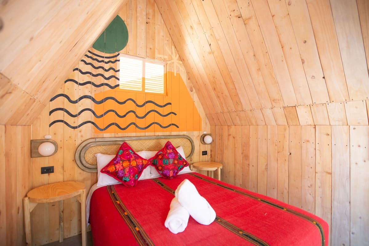 Una habitación de madera con una cama, almohadas y una pequeña mesa.