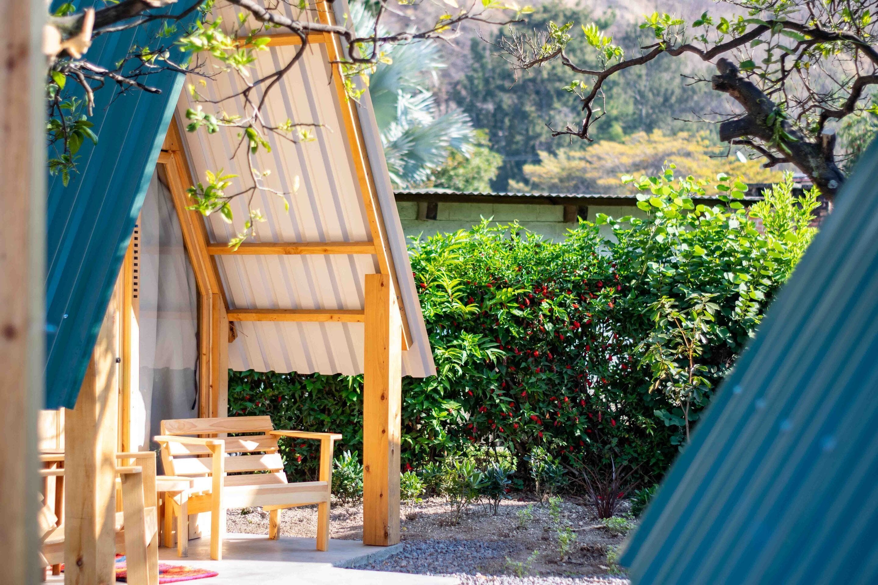 A wooden structure with a slanted roof, surrounded by greenery and a small garden area.