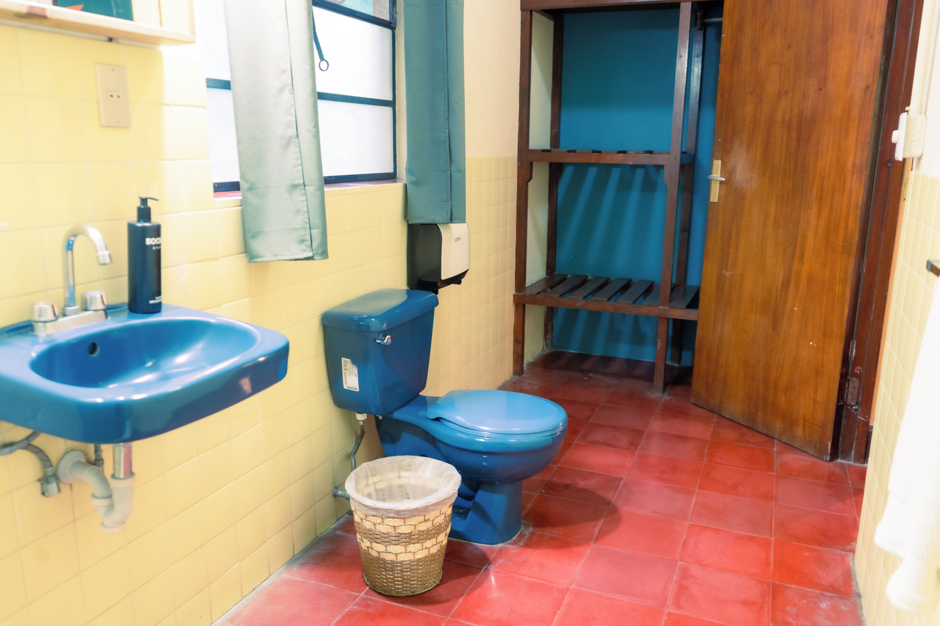 Un baño con lavamanos azul, inodoro y estante de madera.