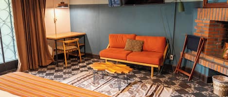 A room with a sofa, a bed, a table, and a TV mounted on the wall.