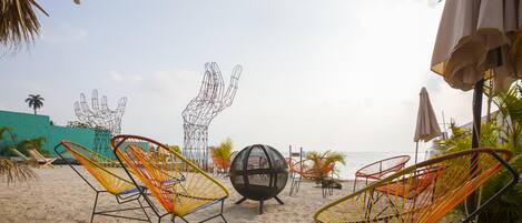 A beach with colorful wire mesh chairs, a spherical sculpture, and umbrellas.