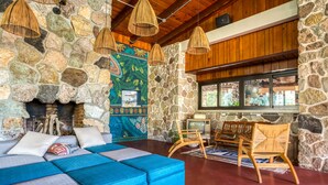 A cozy living area with a stone wall, a blue sectional sofa, wicker chairs, and a fireplace. - Socialtel Atitlan (Panajachel)