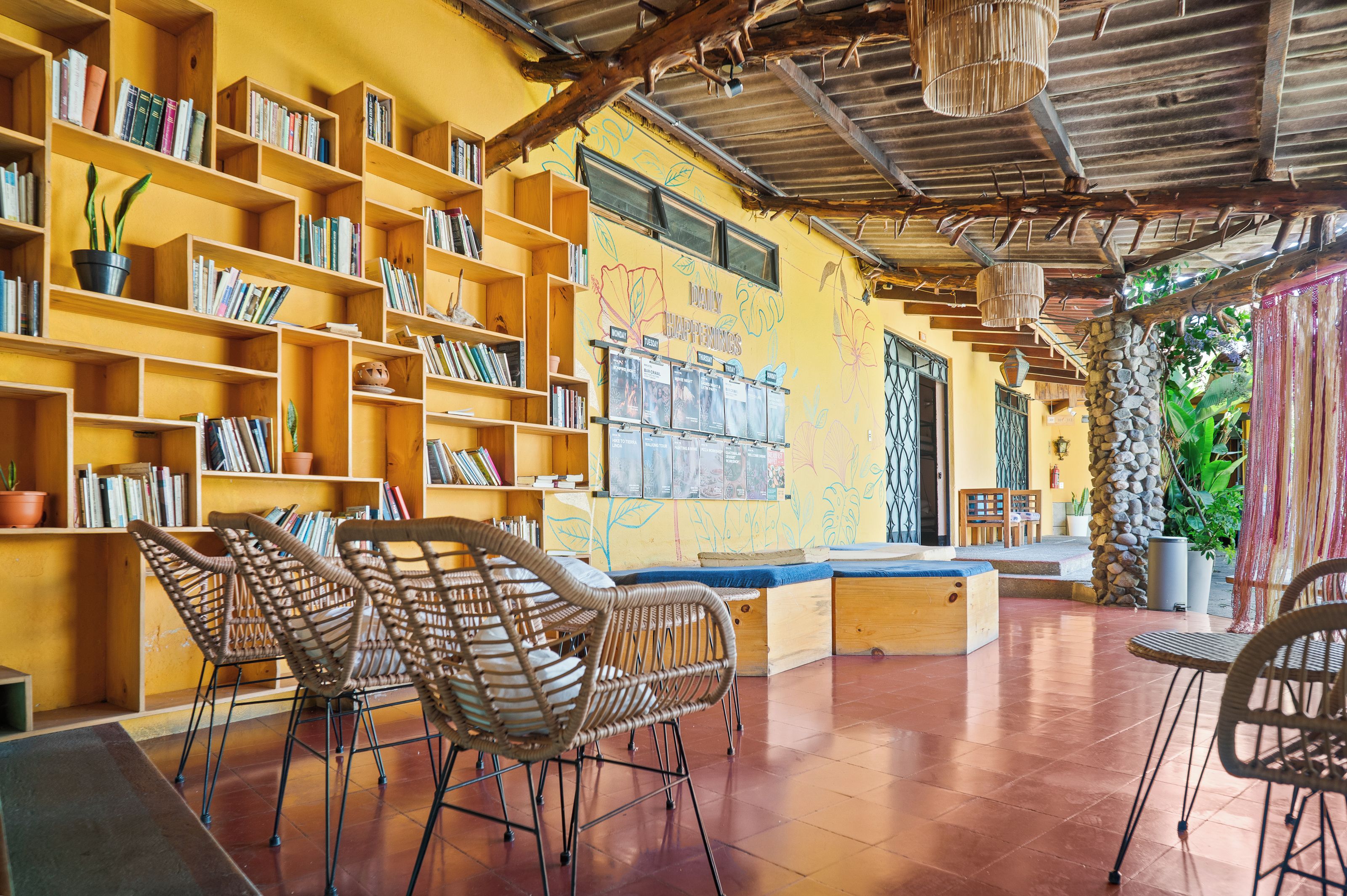 Une bibliothèque avec des étagères, des fauteuils en osier et une fresque murale.