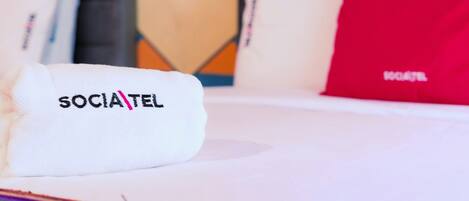 A hotel bed with a white pillow labeled 'SOCIATEL' and a red pillow in the background.