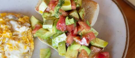 A breakfast plate with toast topped with diced tomatoes, cucumbers, and herbs, alongside scrambled eggs and a cup of coffee on a wooden table.