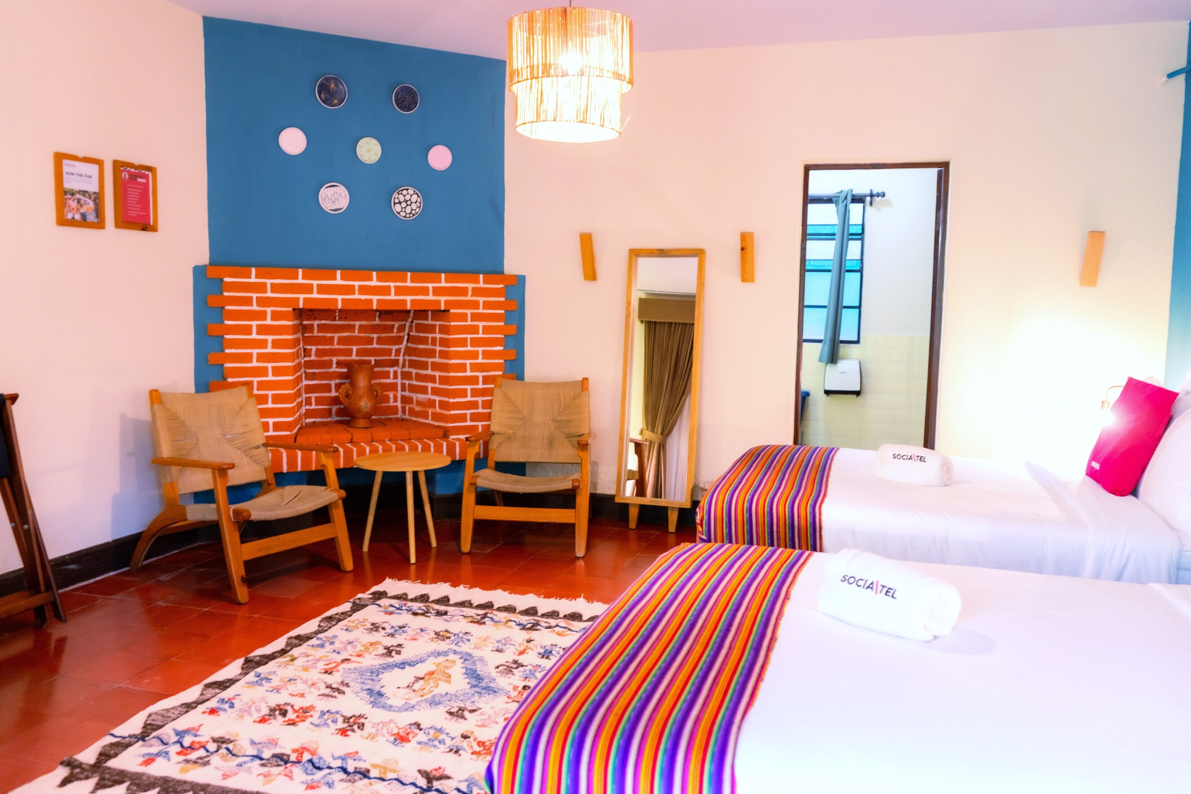 Una habitación de hotel con chimenea de ladrillo, dos camas, un espejo y una silla de madera.