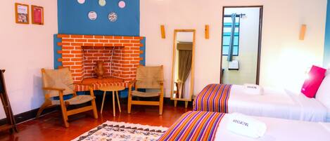 Una habitación de hotel con chimenea de ladrillo, dos camas, un espejo y una silla de madera.