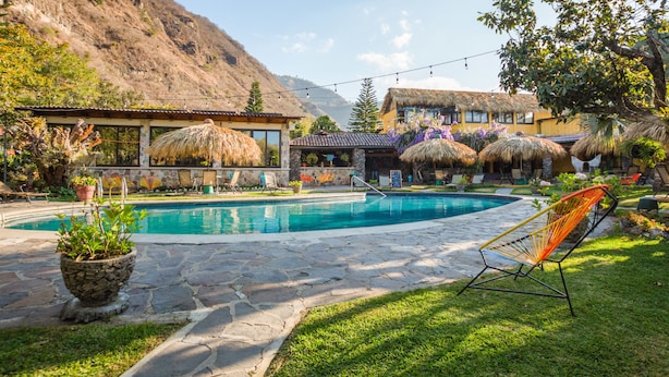 A pool area with stone flooring, lounge chairs, and a mountain backdrop. - Socialtel Atitlan (Panajachel)