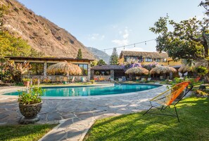 Un espace piscine doté d’un sol en pierre, de chaises longues et offrant une vue sur les montagnes.