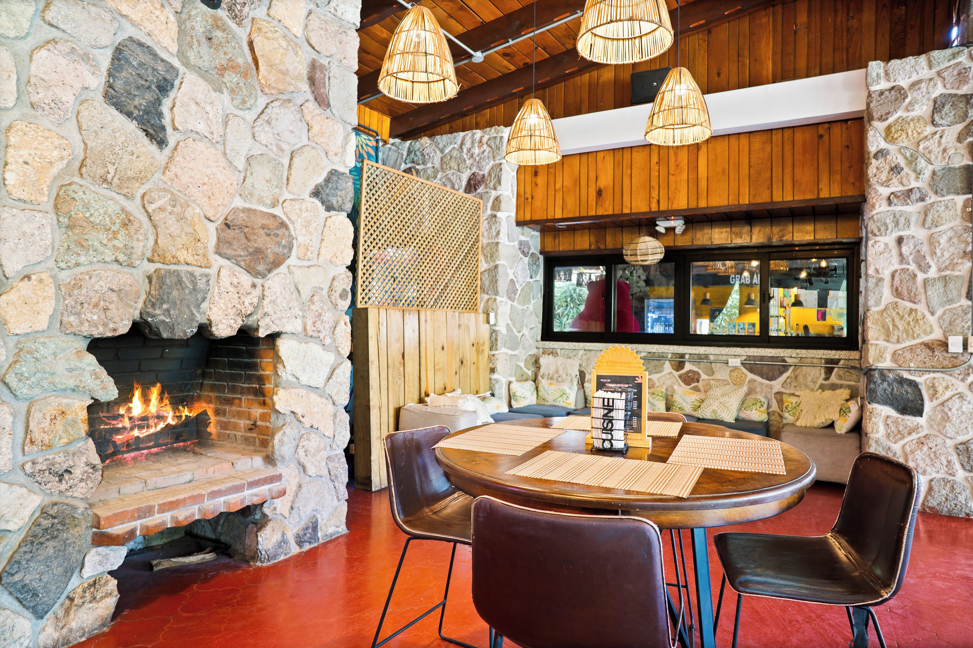 A stone fireplace with a fire, a wooden ceiling, and a round table with chairs.