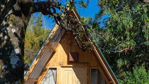 A wooden cabin with a sloped roof, a wooden door, and a small porch area with a bench. - Socialtel Atitlan (Panajachel)