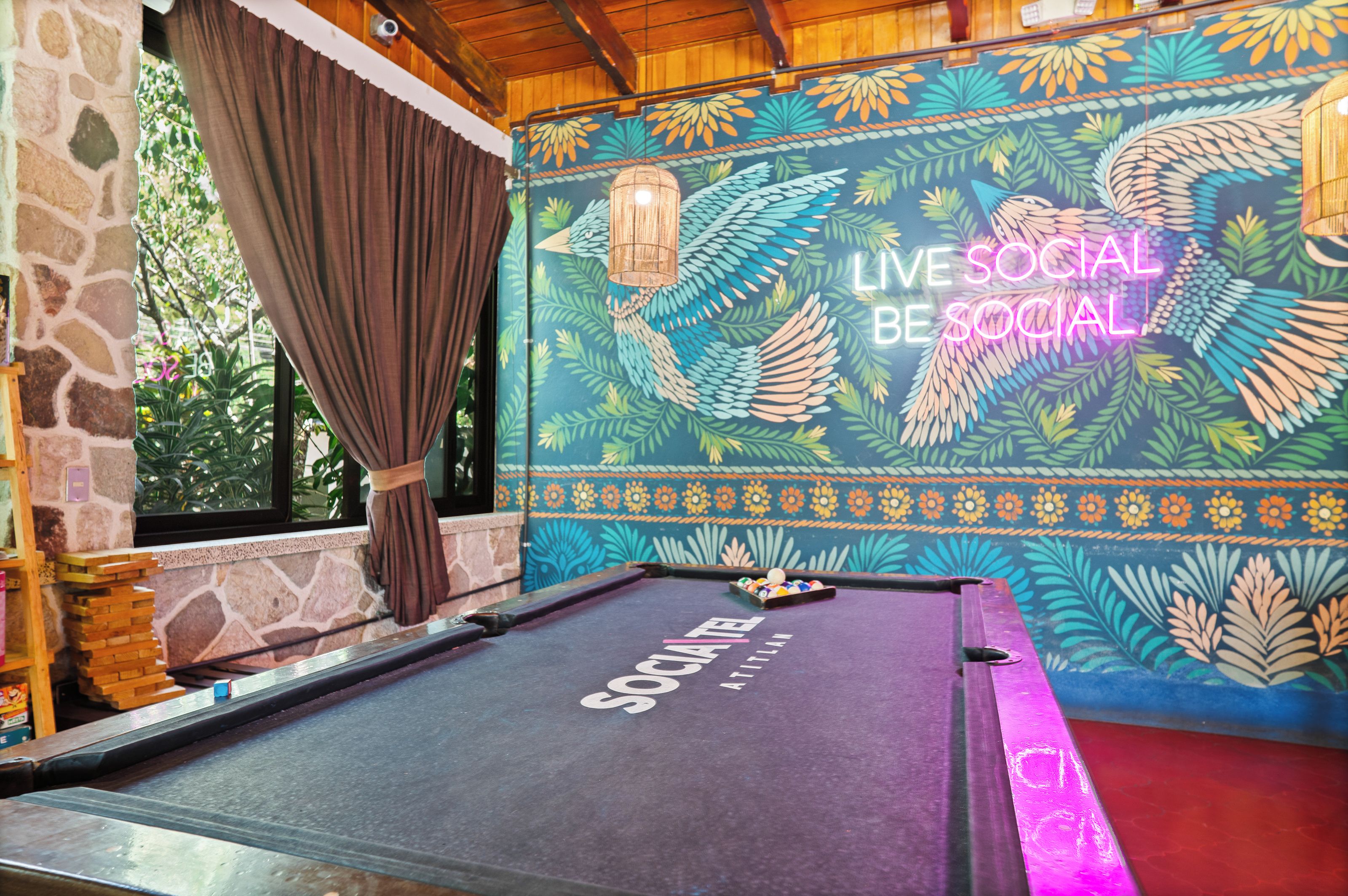 A pool table with a colorful mural in the background and a stone wall on one side.