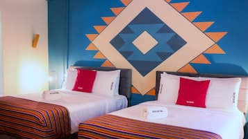 Dos camas individuales con ropa de cama a rayas, una pared azul con patrón geométrico y almohadones con el nombre de marca 'SOCIATEL'.
