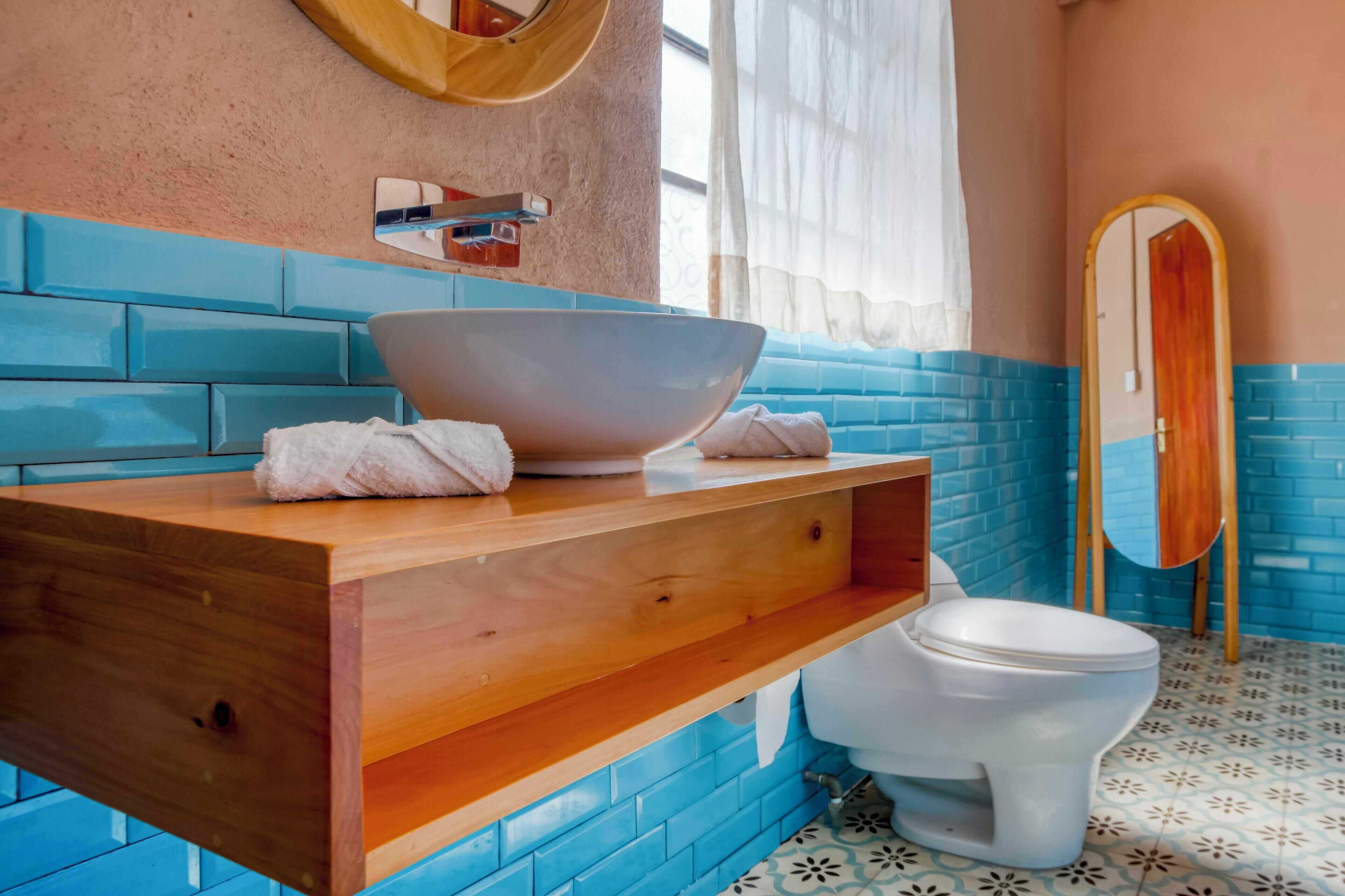A bathroom with a wooden vanity, a large white basin, a white toilet, and a mirror on the wall.