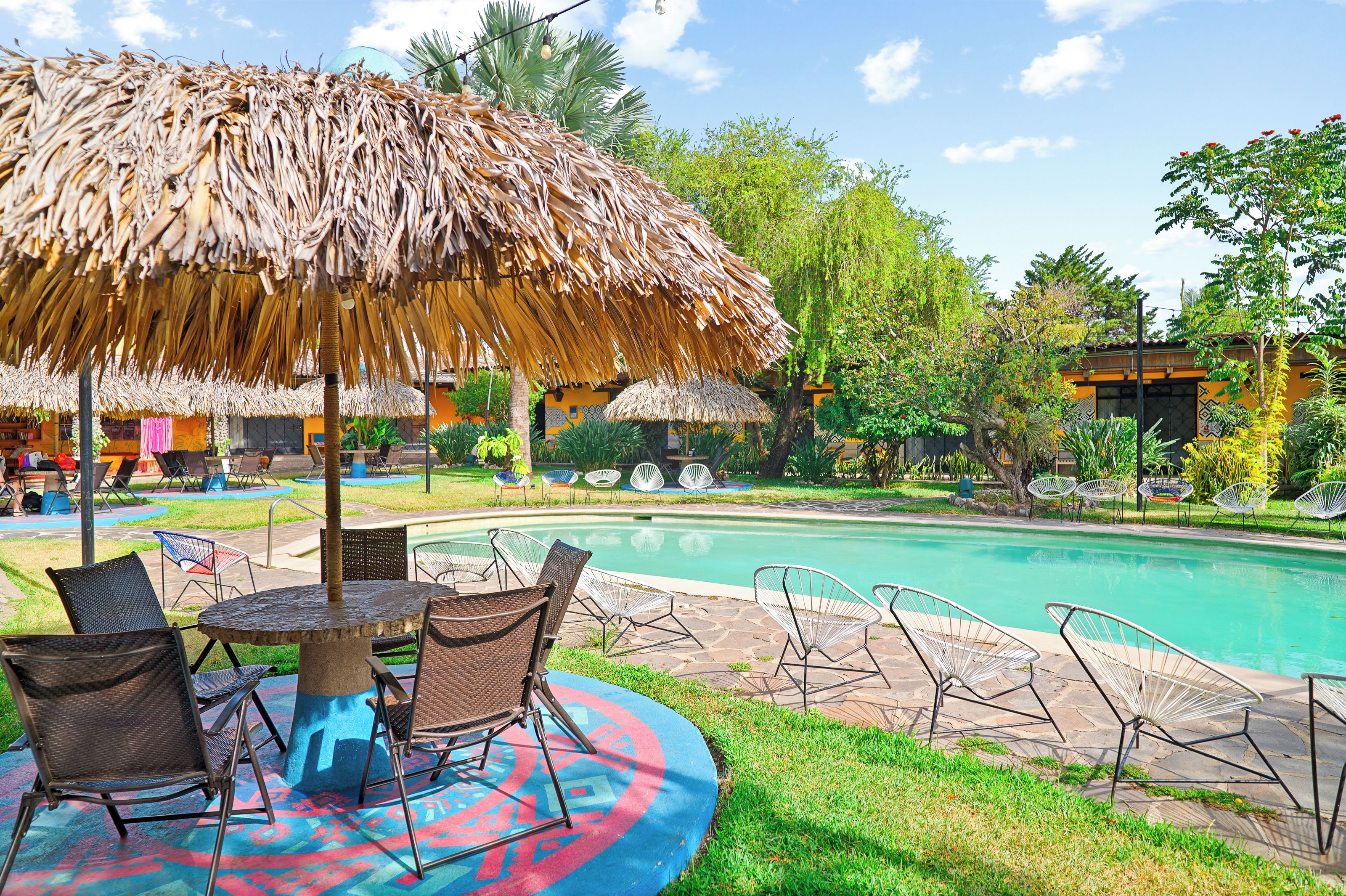 A poolside area with a thatched umbrella, lounge chairs, and a pool.