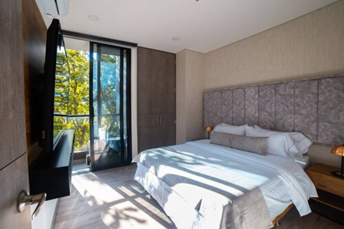 A modern bedroom with a large bed, a sliding glass door to a balcony, and a built-in TV.