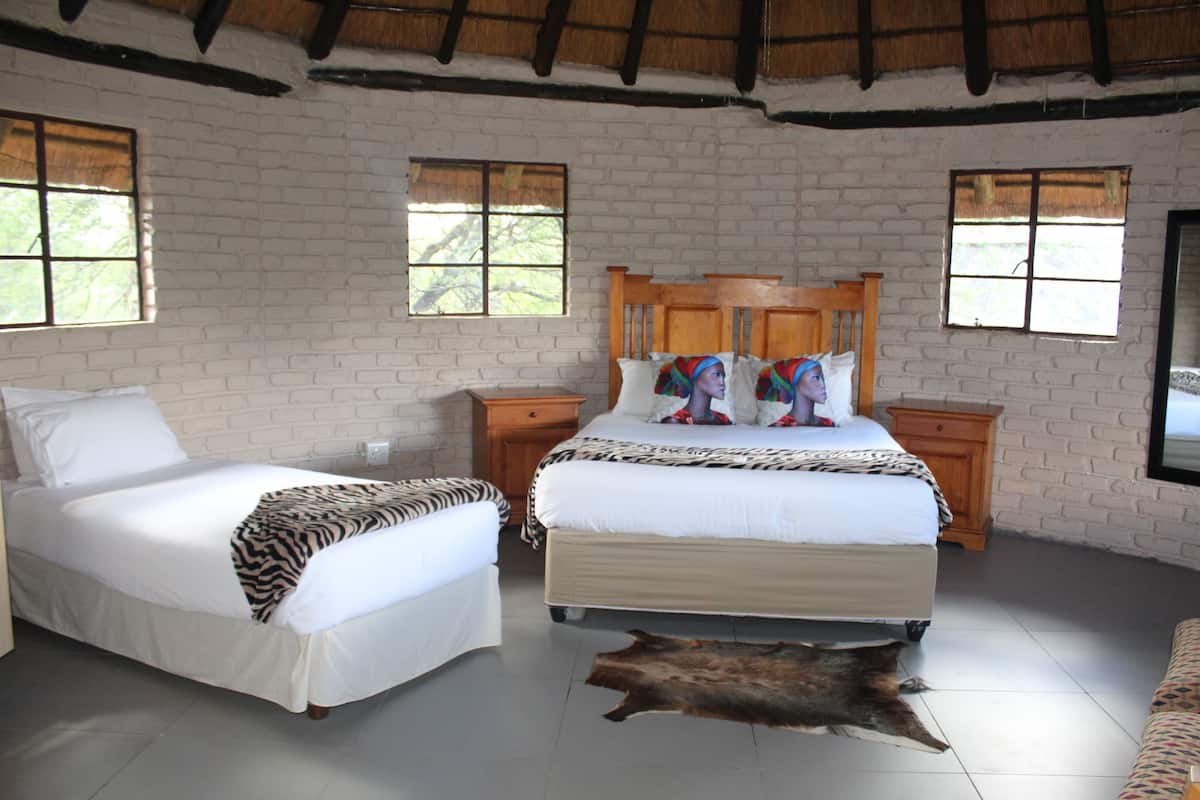 A bedroom with two beds, a wooden headboard, a zebra-patterned blanket, a leather rug, and brick walls.