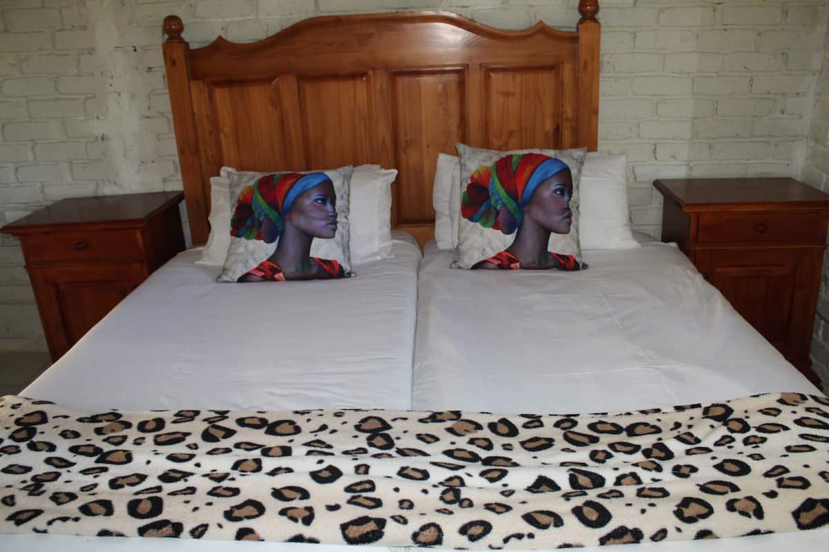A double bed with a leopard print bedspread, two pillows with colorful designs, and a wooden headboard.