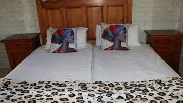 A double bed with a leopard print bedspread, two pillows with colorful designs, and a wooden headboard.