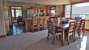 A spacious kitchen with wooden cabinets, a large island, and a dining area with a table and chairs. - Beach Cottages at Lake George (Lake George)