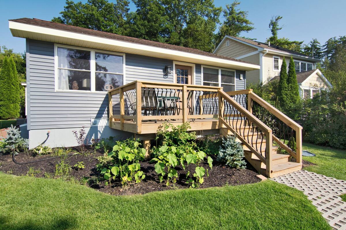 A house with a wooden deck, a staircase, and a garden with various plants.