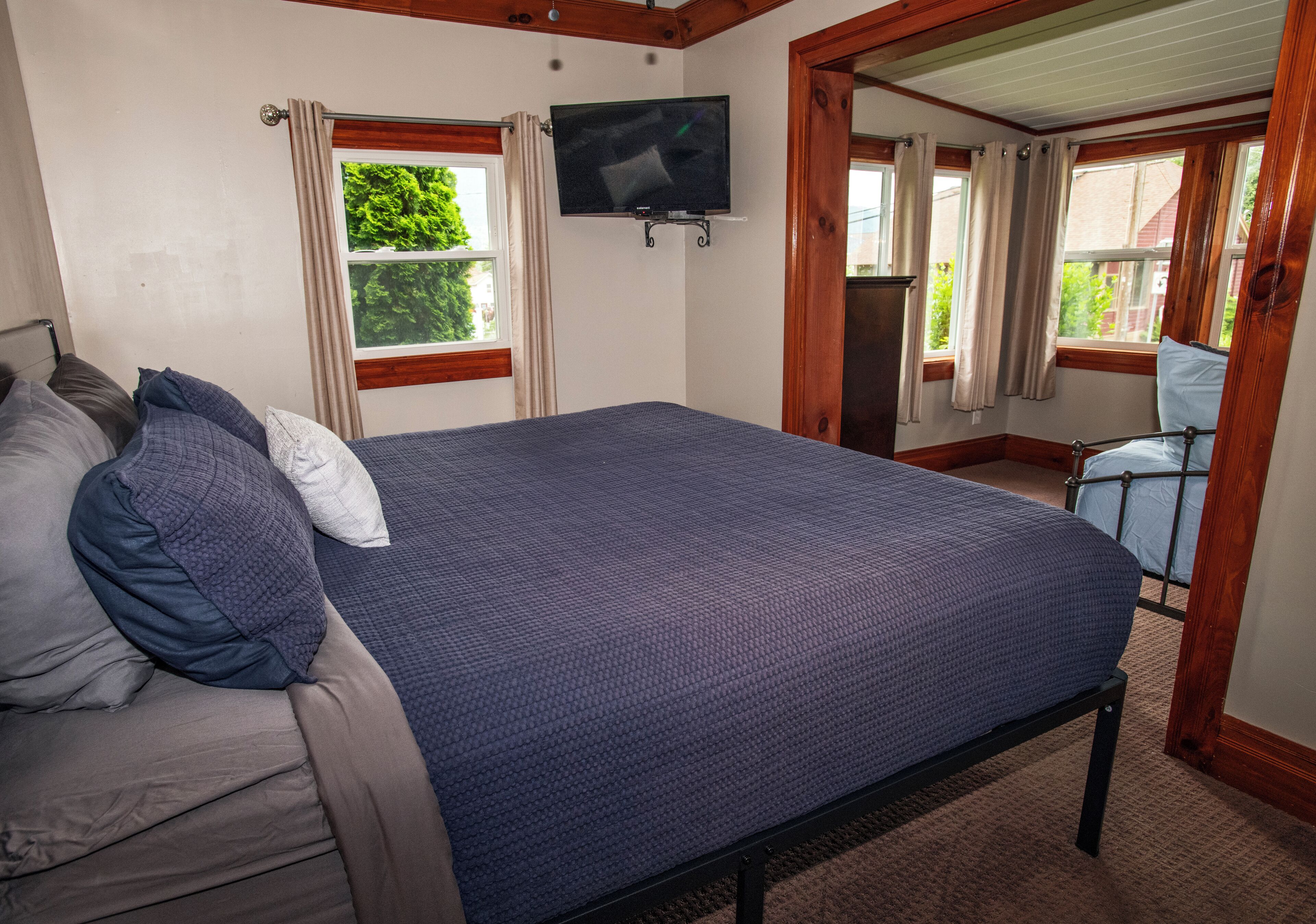 A bedroom with a bed, a television mounted on the wall, and a window with curtains.