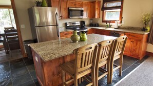 A kitchen with wooden cabinets, a granite countertop, a stainless steel refrigerator, a microwave, and a sink. - Beach Cottages at Lake George (Lake George)