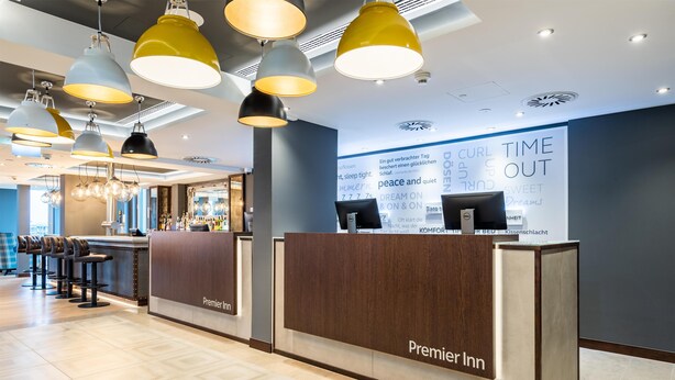 A hotel reception area with a modern design, featuring a reception desk, bar area, and seating. - Premier Inn München City Schwabing (Munich)