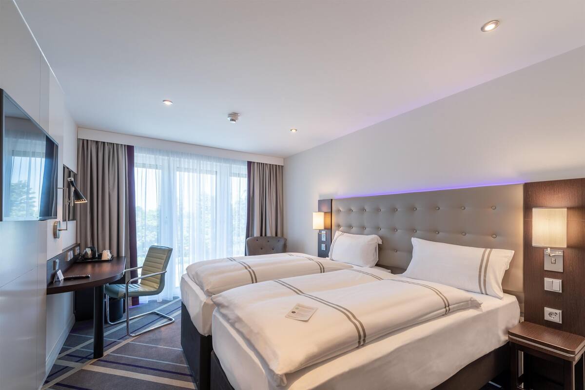 A hotel room with two beds, a desk, a chair, a TV, and a window with curtains.