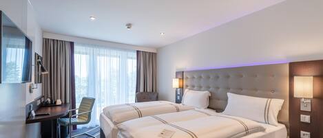 Habitación de hotel con dos camas, un escritorio, una silla, un televisor y una ventana con cortinas.