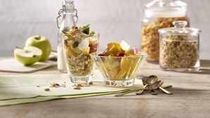 Two glasses of fruit salad with a bottle and jars of granola in the background. - Premier Inn München City Schwabing (Munich)