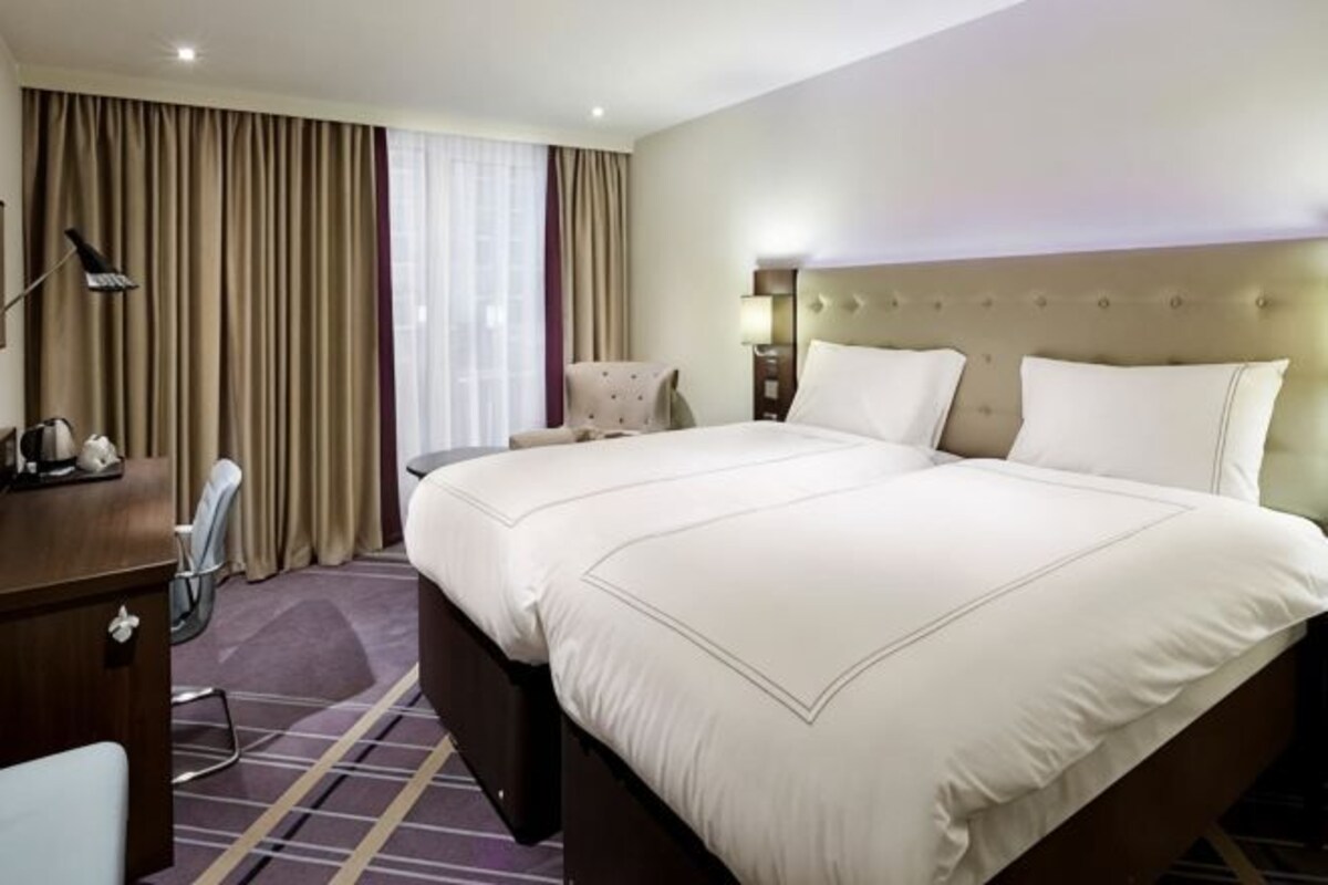 A hotel room with a large bed, a desk, a chair, and a window with curtains.