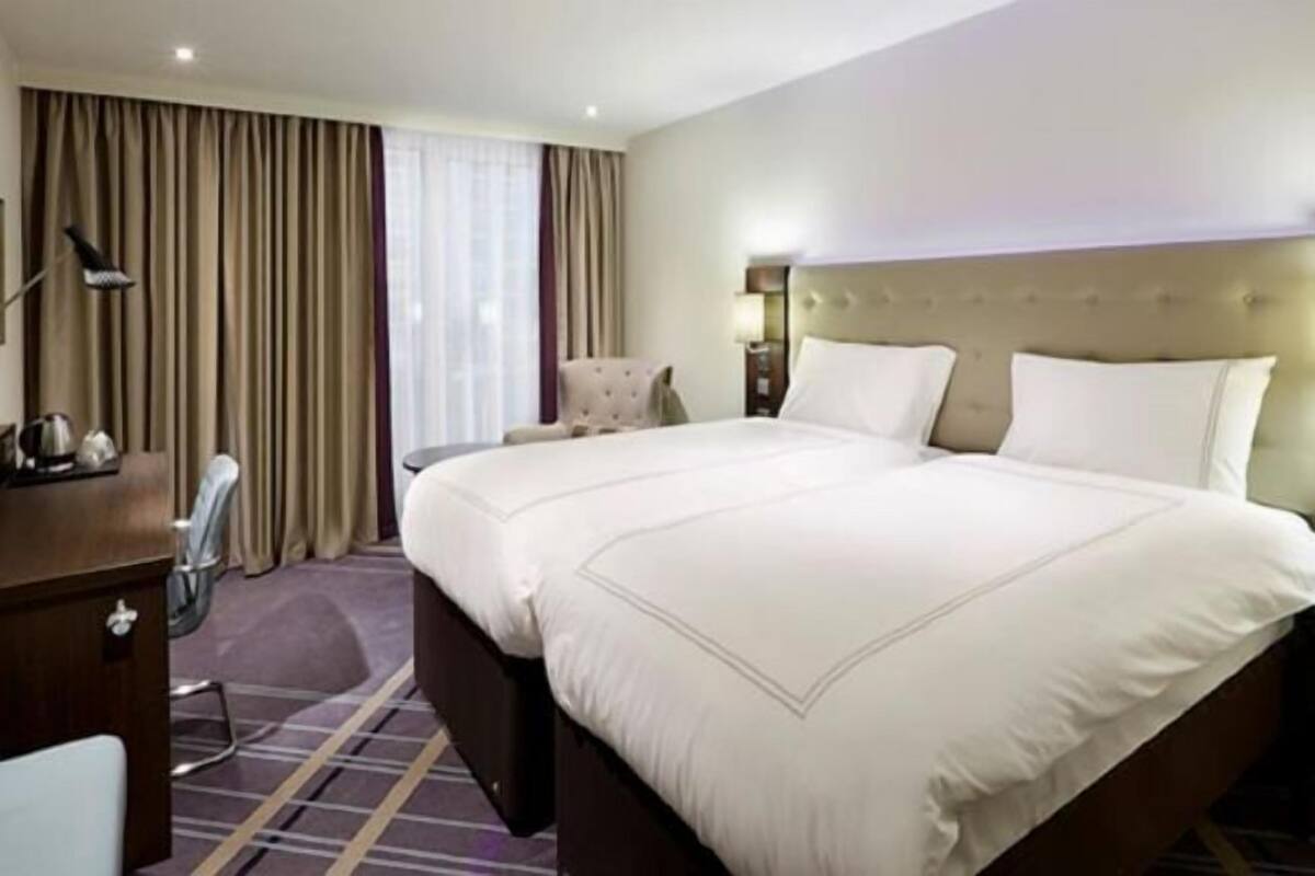 A hotel room with a large bed, a desk, a chair, and a window with curtains.