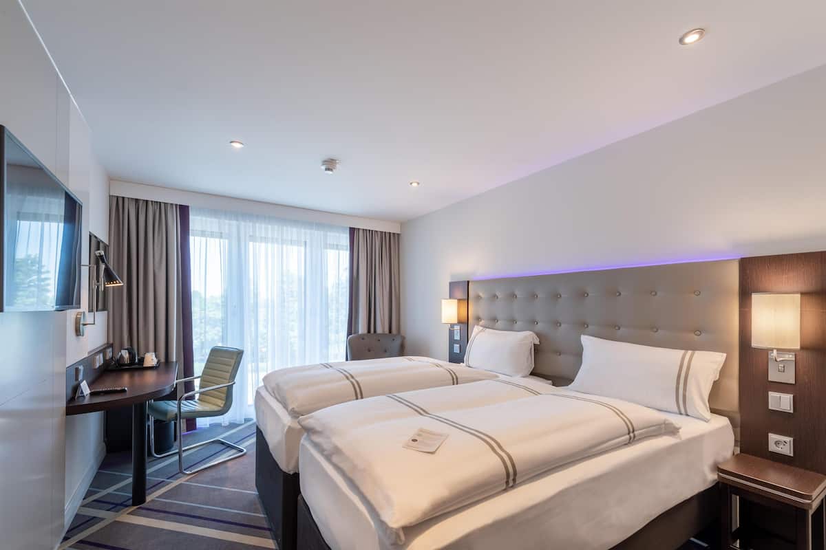 Une chambre d’hôtel avec deux lits, un bureau, une chaise, une télévision et une fenêtre avec des rideaux.